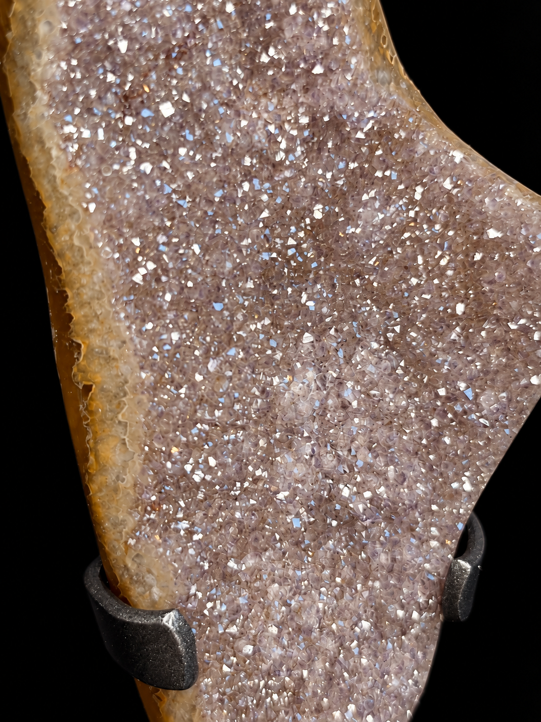 A close-up of a natural druzy crystal specimen with sparkling quartz flecks over a warm brown and tan base, photographed against a black background.