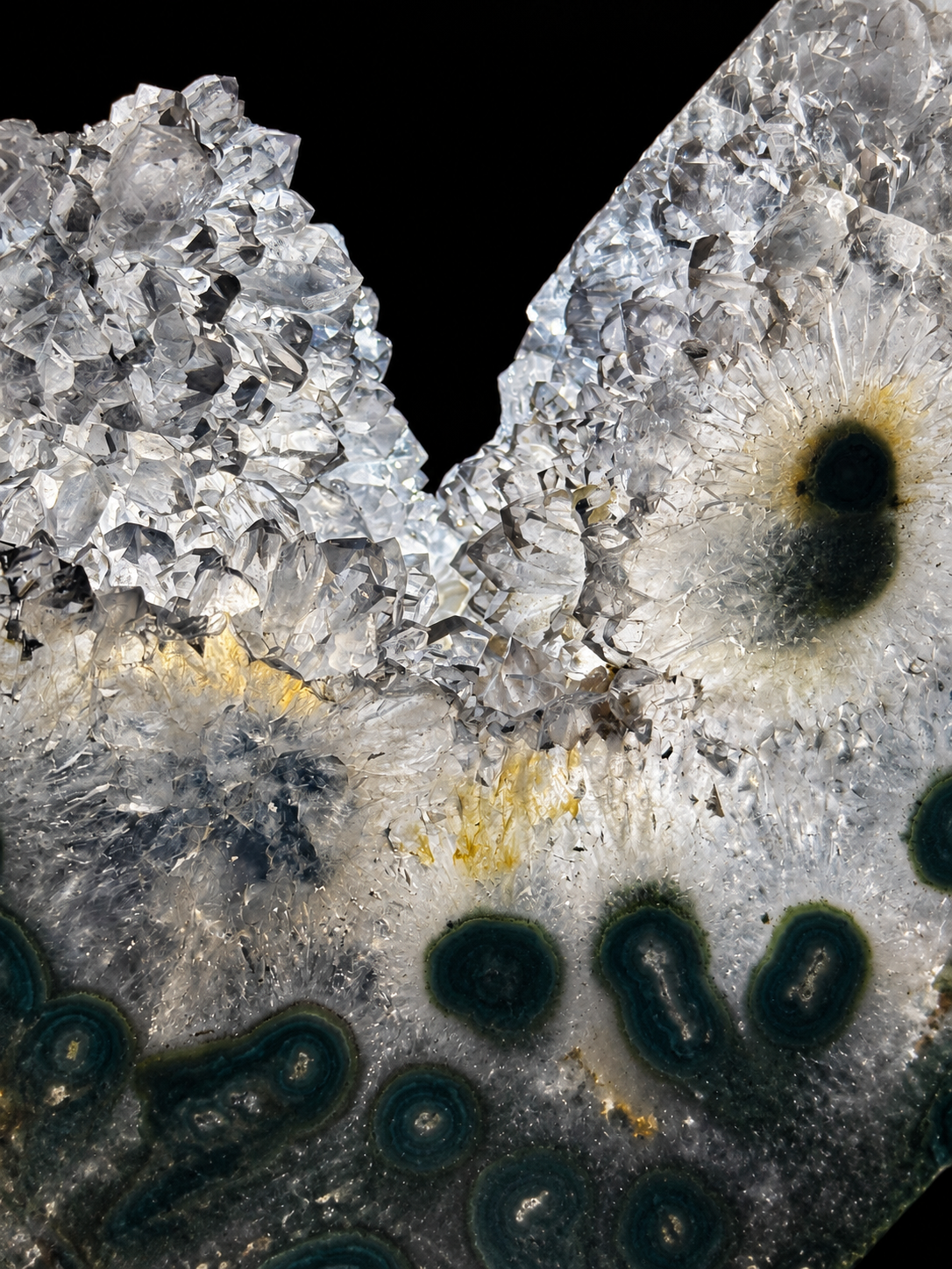 A close-up of a mineral specimen with dense translucent quartz crystals dark green concentric stalactite "eyes", and small yellow mineral inclusions against a black background.