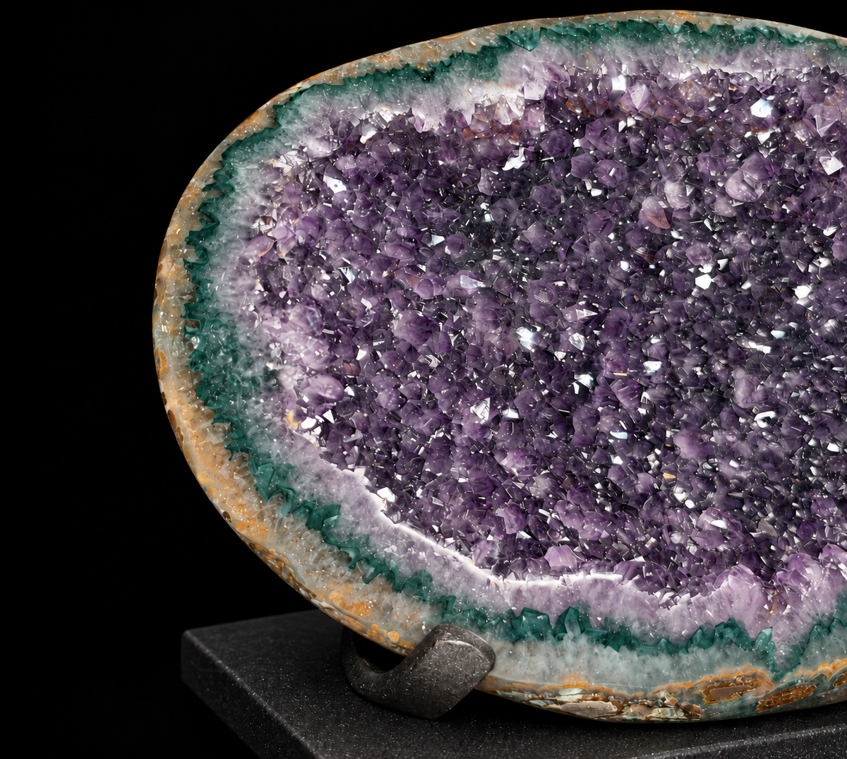 A polished amethyst geode dome with a dark green and white banded outer edge, displayed on a black stand against a solid black background.