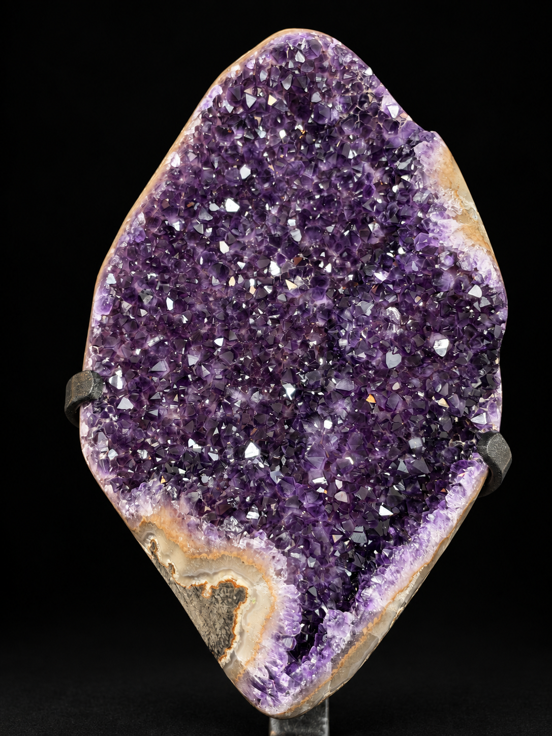 A raw amethyst geode specimen with a deep purple crystal cavity and natural tan-brown outer matrix, displayed on a stand against a black background.