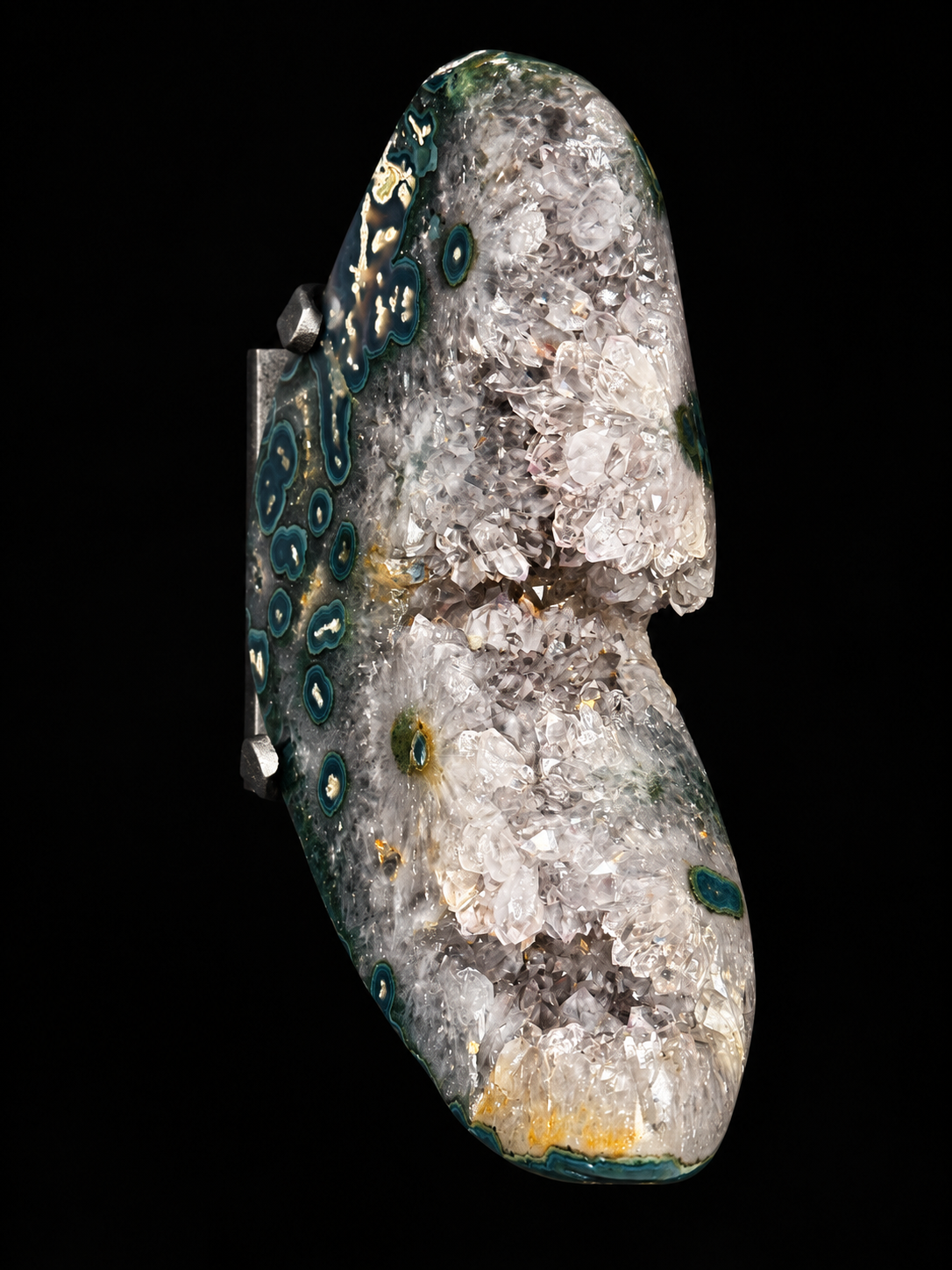 A polished top down view of a natural quartz and agate specimen accented by dark teal circular patterns on one side and small yellow-green areas visible as well, shown against a solid black background.